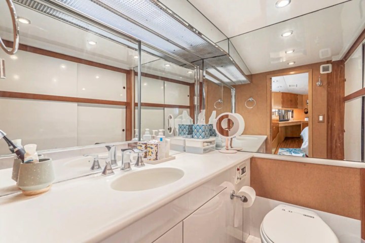 Modern bathroom with large mirror, sink, and toilet on a yacht, reflecting a cabin entrance.