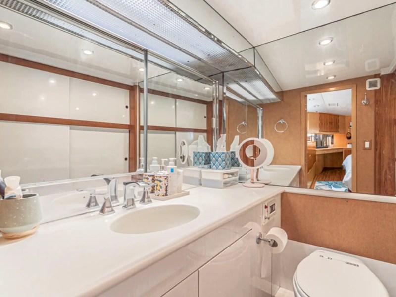 Modern bathroom with large mirror, sink, and toilet on a yacht, reflecting a cabin entrance.
