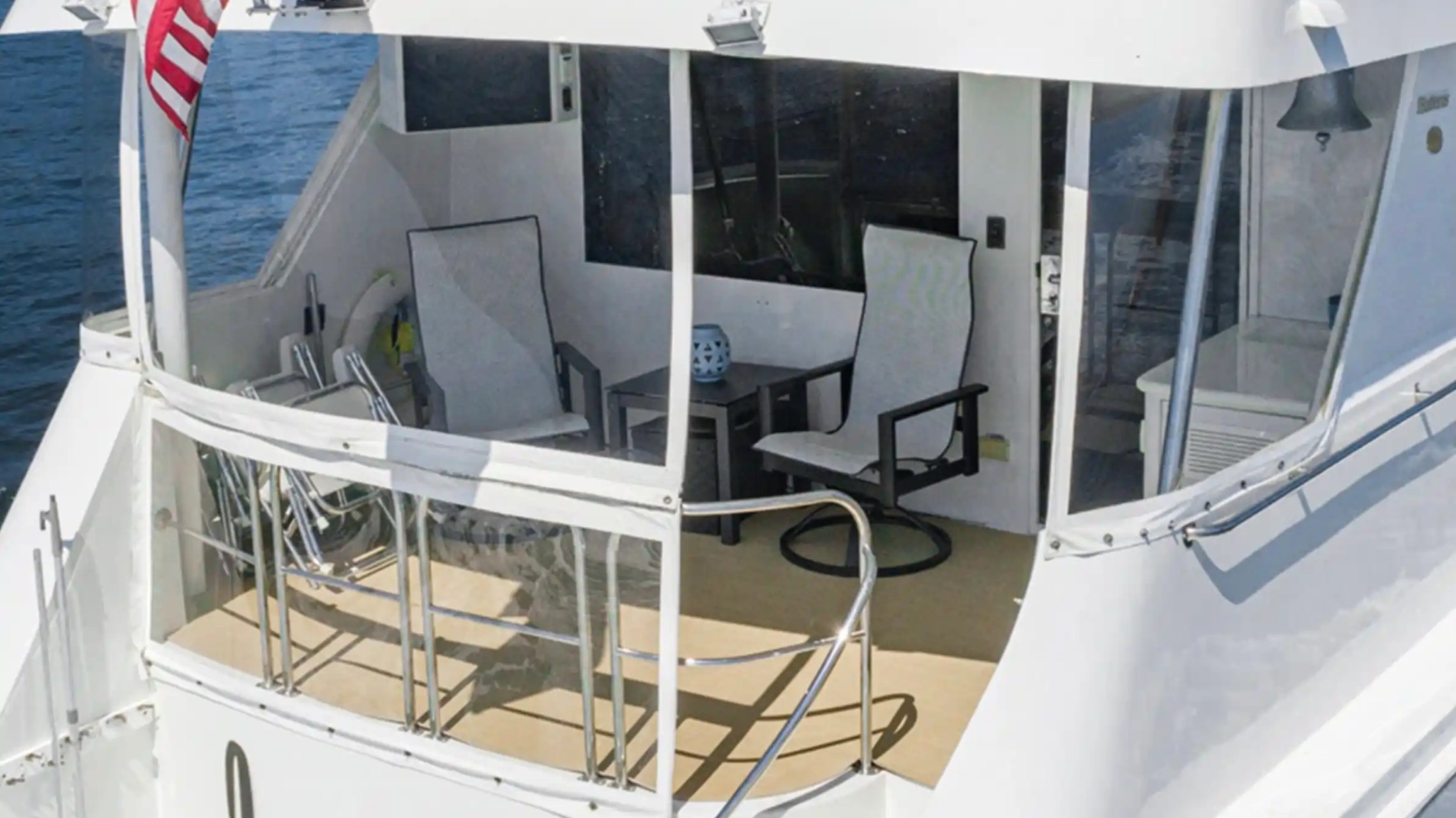 Back view of a yacht deck with chairs, table, and American flag.