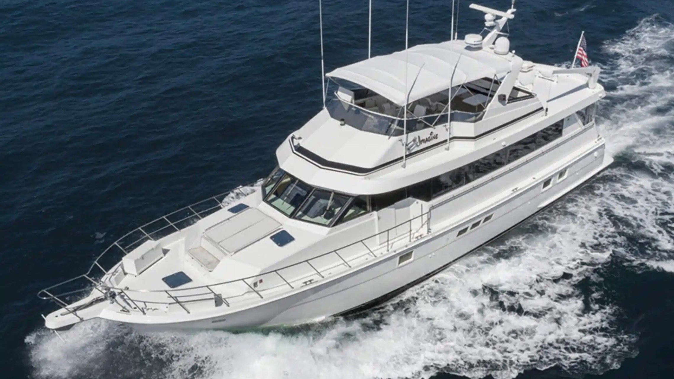 White yacht cruising on the ocean with visible wake behind it.