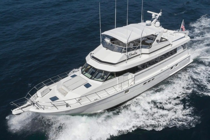 White yacht cruising on the ocean with visible wake behind it.