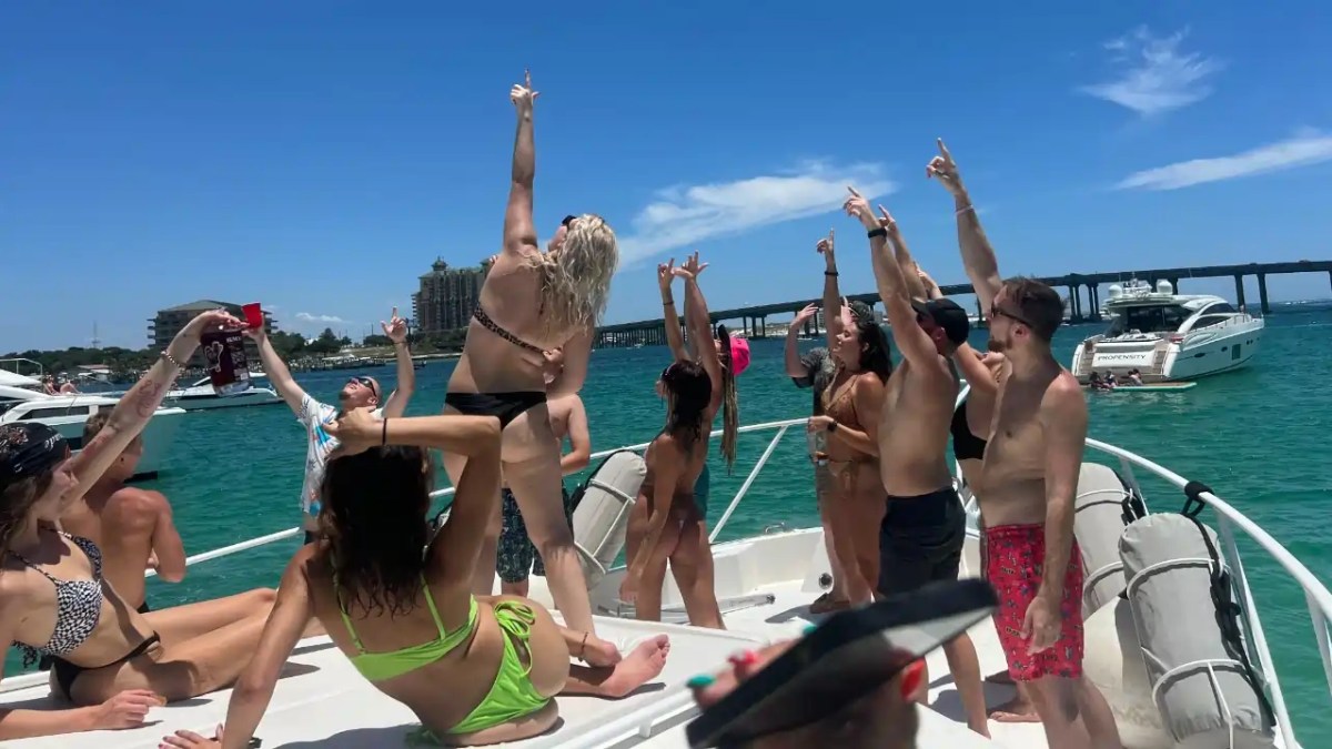 Group of people partying on a boat under a sunny sky with other boats in the background.