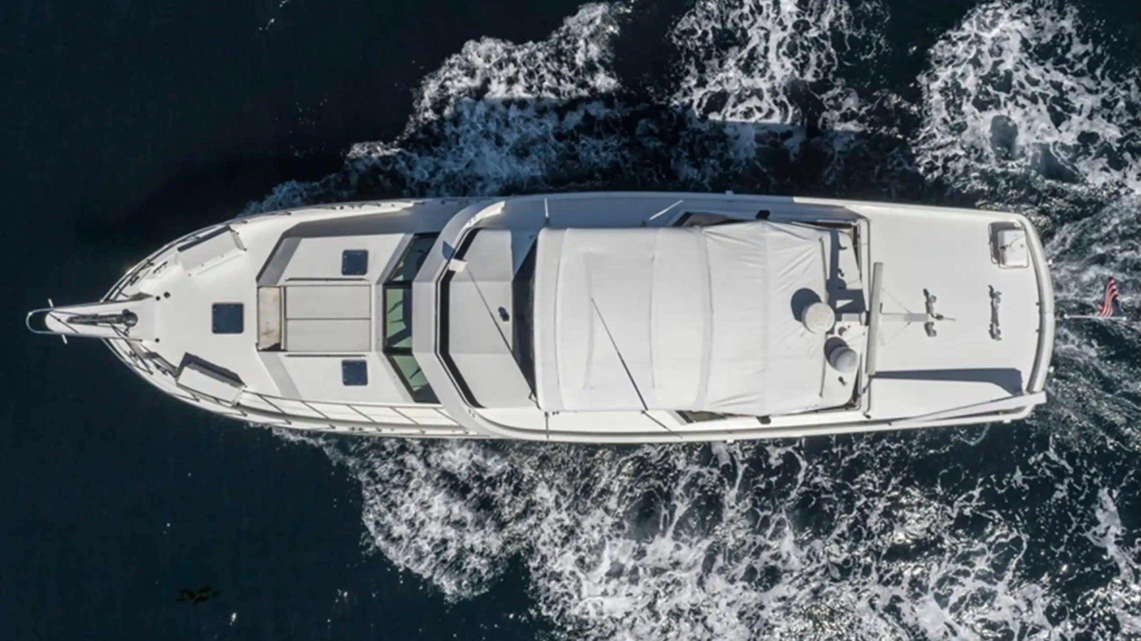 Aerial view of a white yacht moving through dark blue water with white waves.