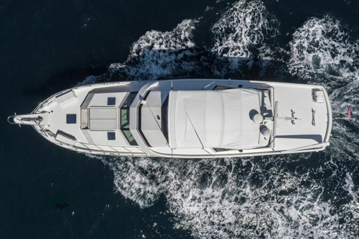 Aerial view of a white yacht moving through dark blue water with white waves.
