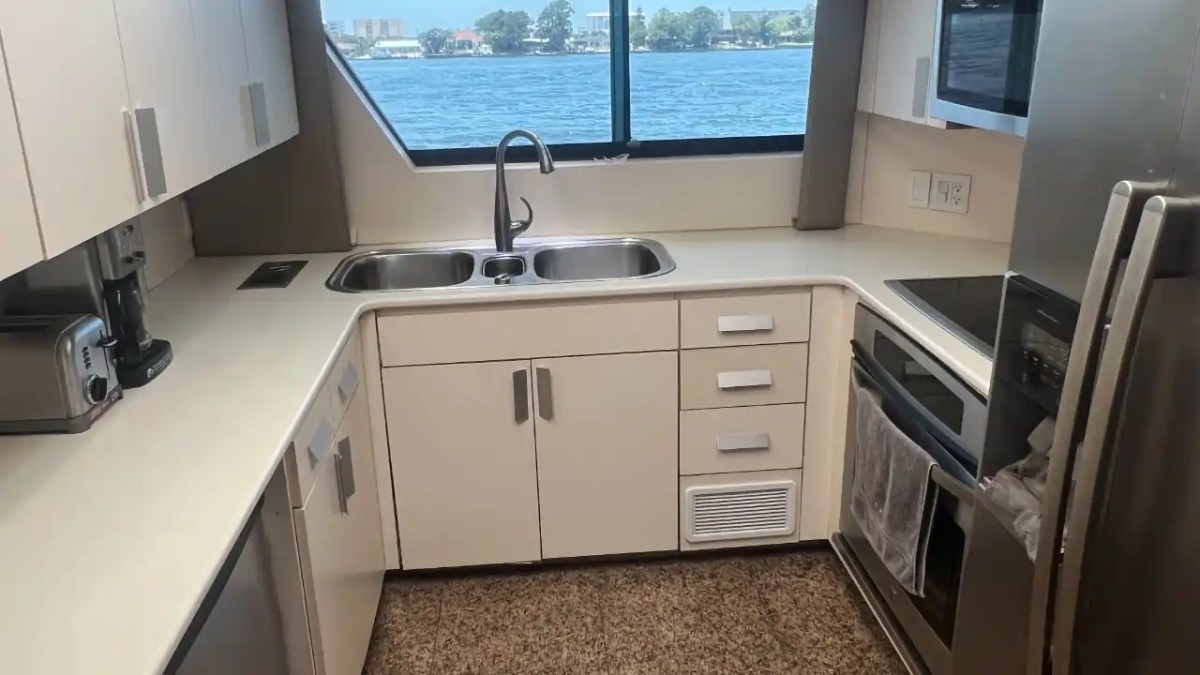 L-shaped kitchen with white cabinets, double sink, and large window overlooking water.