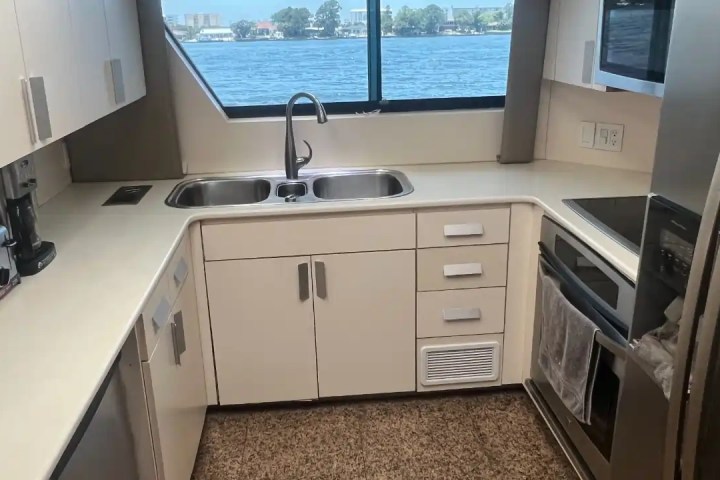 L-shaped kitchen with white cabinets, double sink, and large window overlooking water.