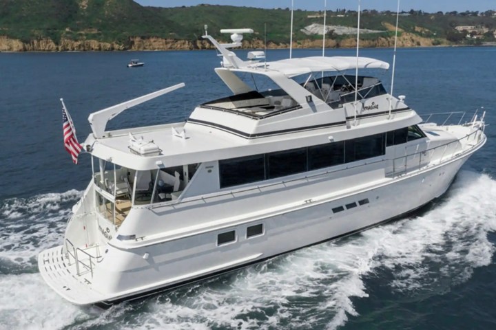 White yacht cruising in ocean near cliffs, with American flag at stern.