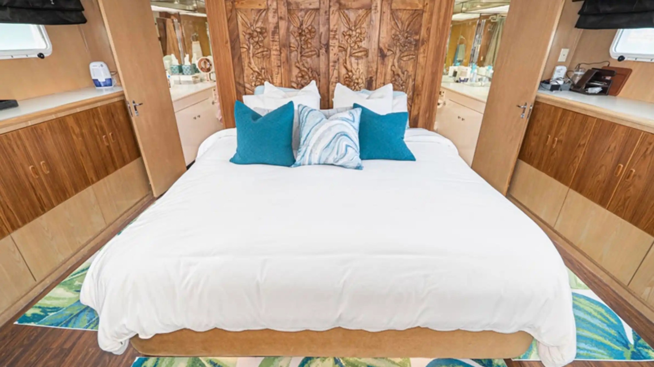 Bedroom with carved wooden headboard, white bedding, blue pillows, and wood cabinets.