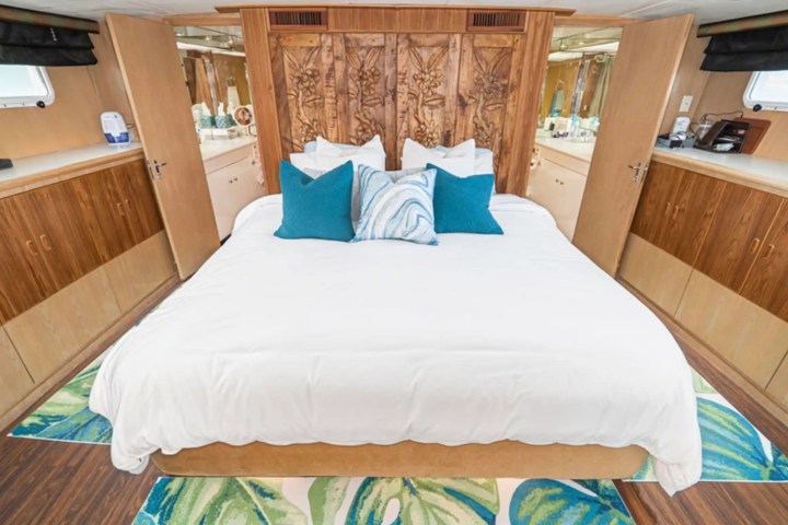 Bedroom with carved wooden headboard, white bedding, blue pillows, and wood cabinets.