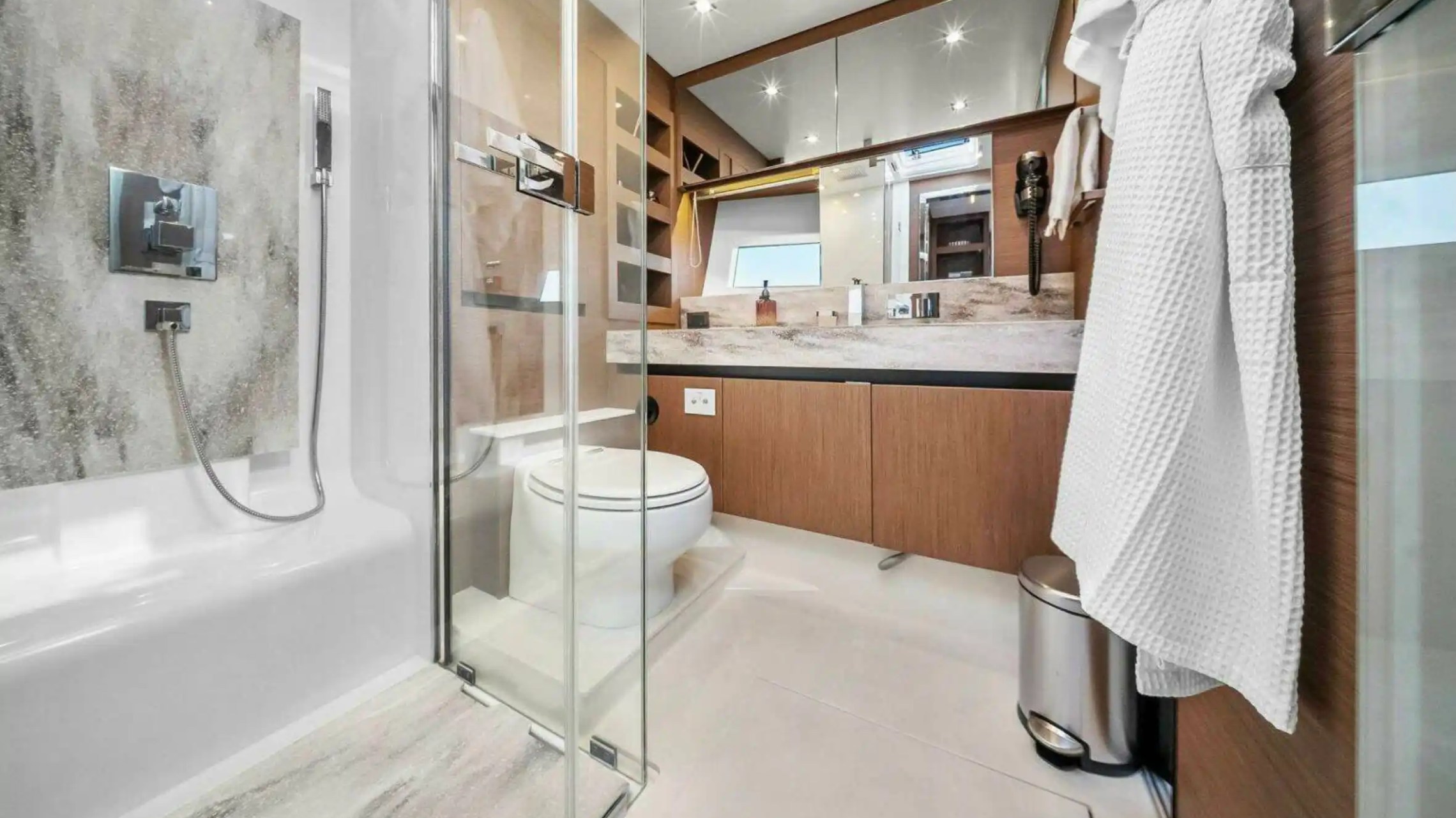 Modern bathroom with glass shower, wood cabinets, and wall mirror.