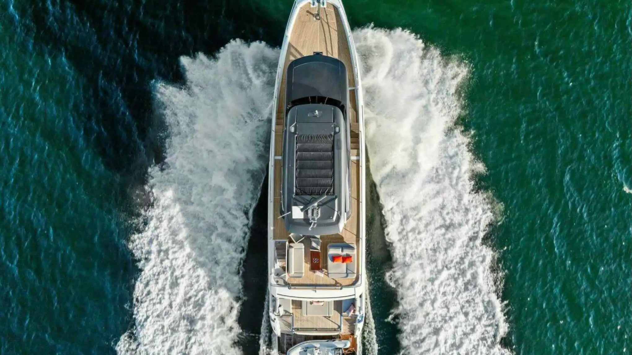 Aerial view of a yacht moving through blue-green water, leaving a wake behind.