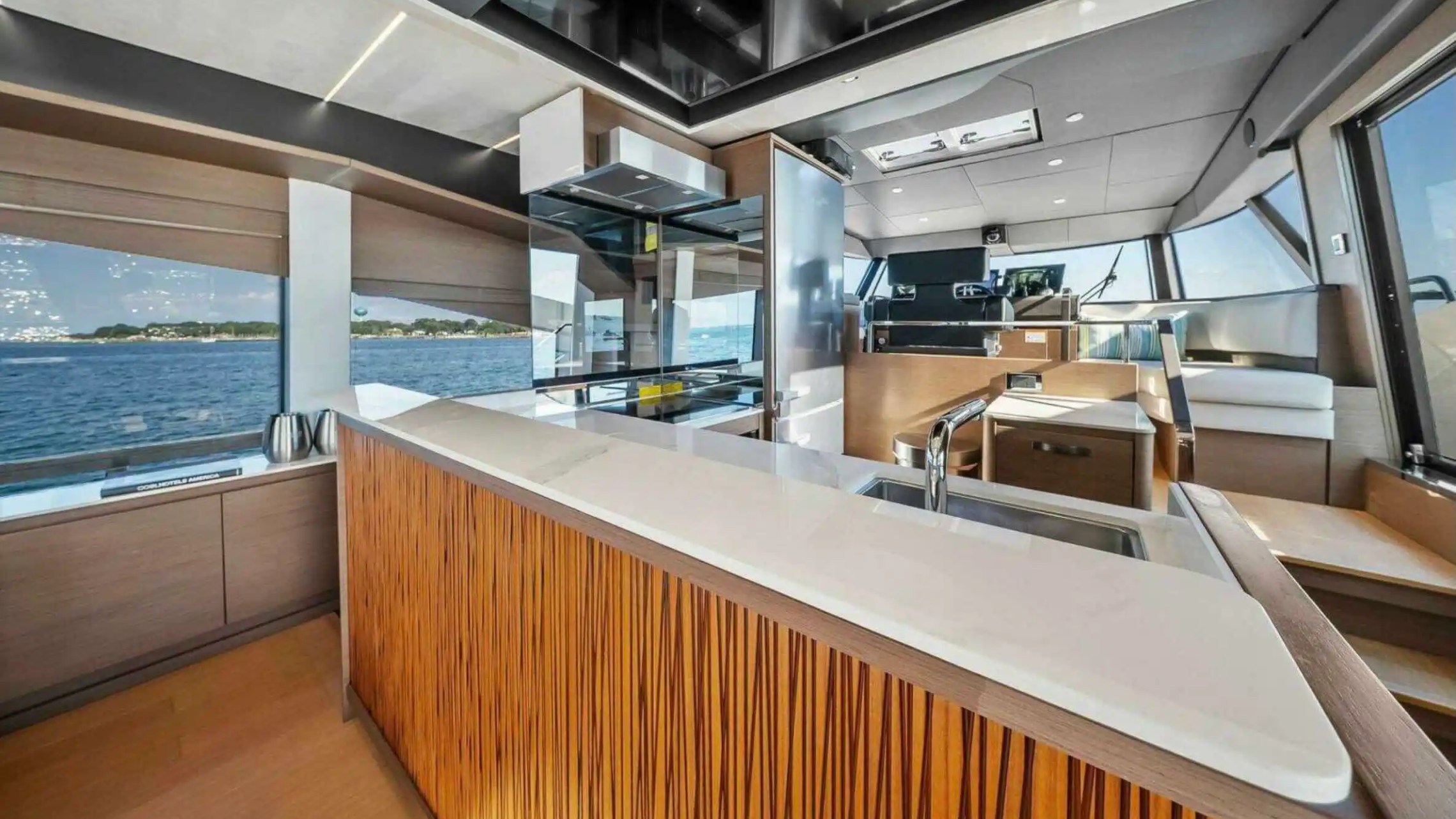 Modern yacht interior with kitchen, sink, and seating, overlooking ocean through large windows.