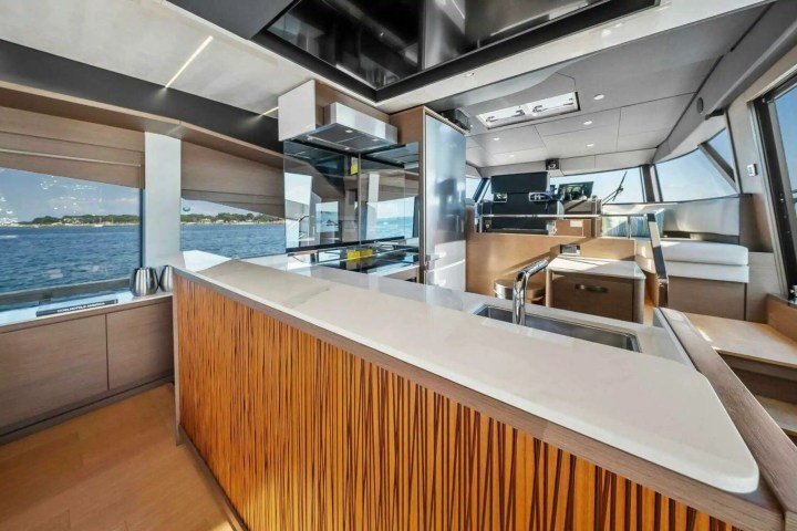 Modern yacht interior with kitchen, sink, and seating, overlooking ocean through large windows.