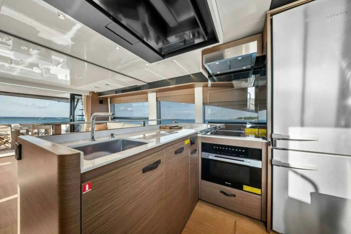 Modern yacht kitchen with stainless steel appliances and ocean view through large windows.