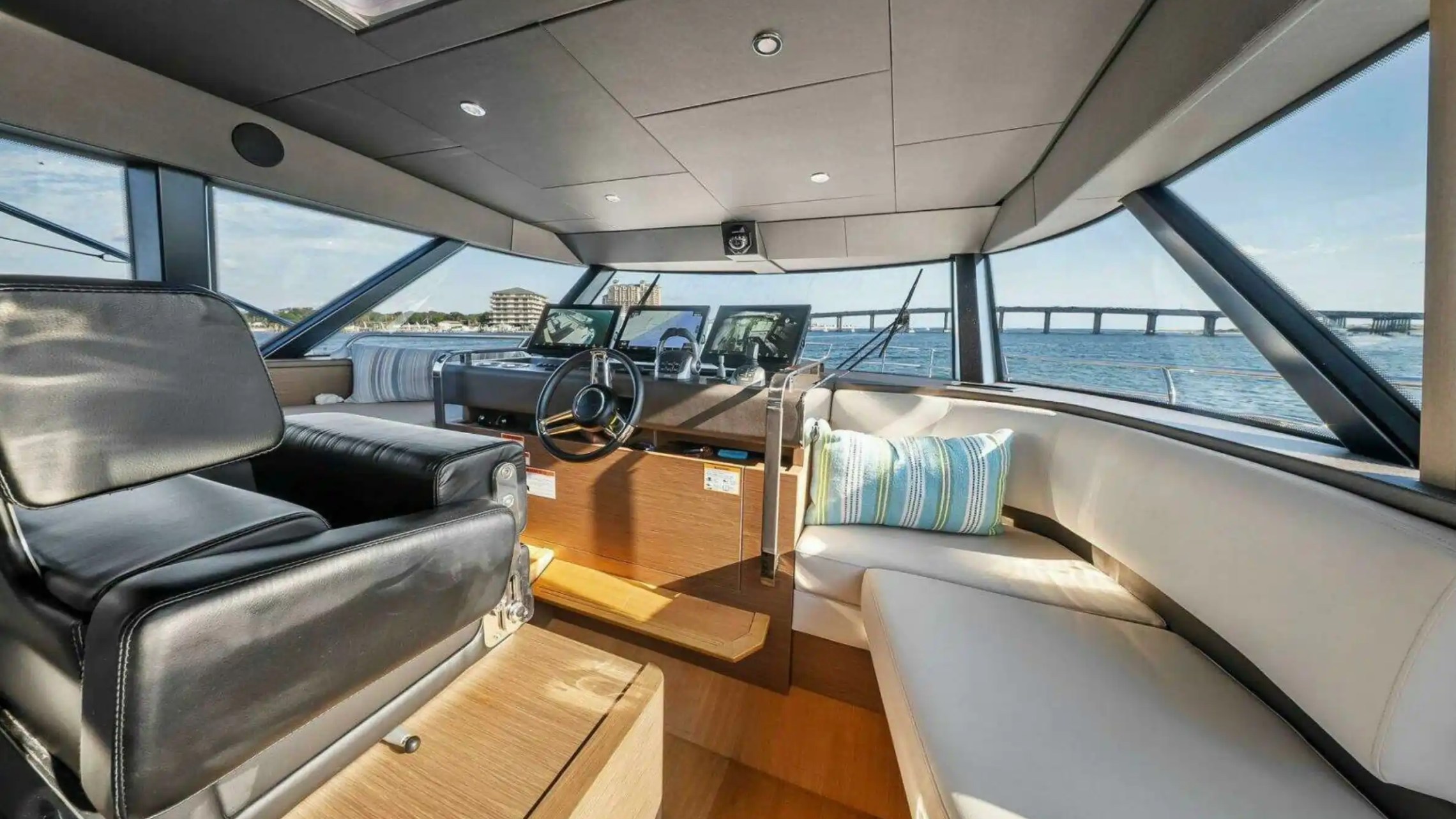 Interior of a yacht cabin with steering wheel, black seat, and blue striped pillows.