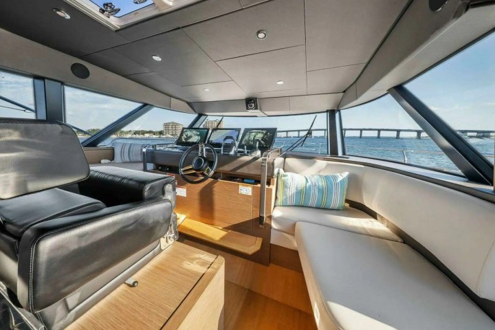 Interior of a yacht cabin with steering wheel, black seat, and blue striped pillows.