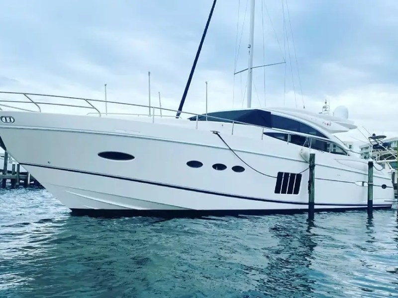 White yacht docked on calm water with overcast sky in the background.