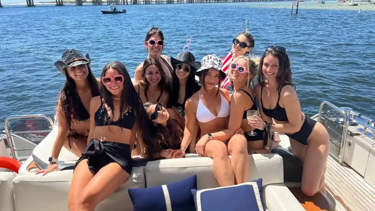 Group of women in swimwear posing on a boat with a bridge in the background.