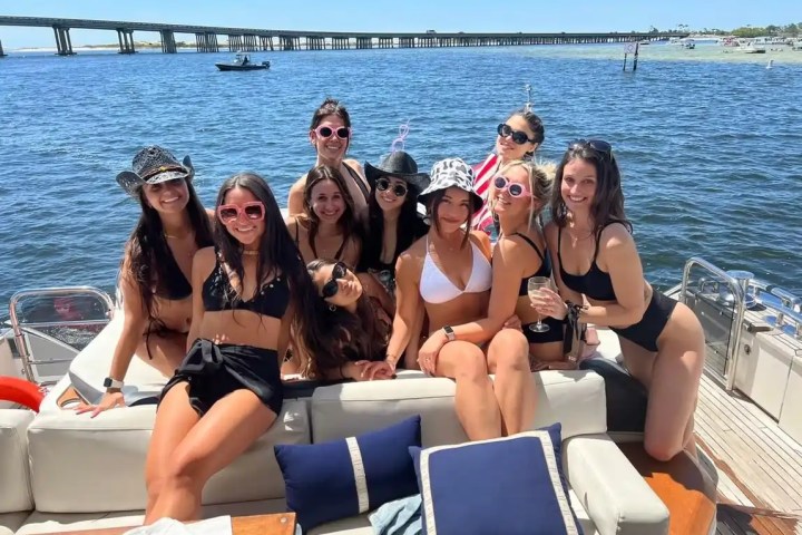 Group of women in swimwear posing on a boat with a bridge in the background.