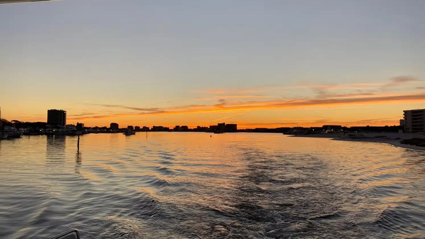 Sunset view from a boat, with buildings outlined against an orange sky.