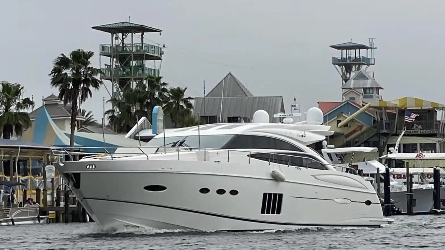 A large white yacht docked near colorful waterfront buildings and palm trees.
