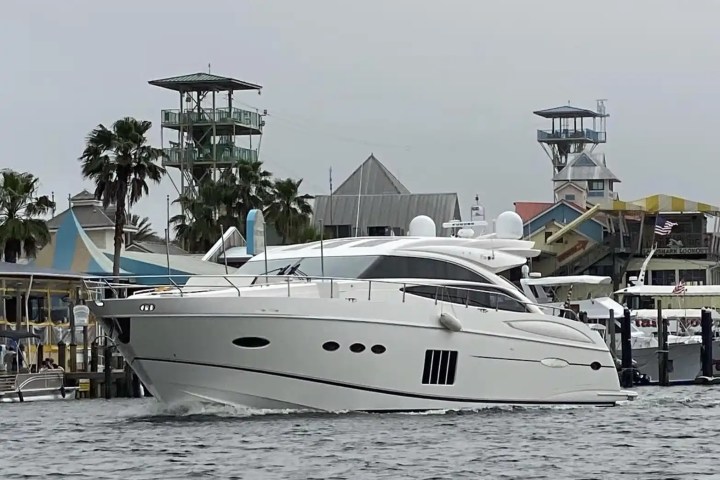 A large white yacht docked near colorful waterfront buildings and palm trees.