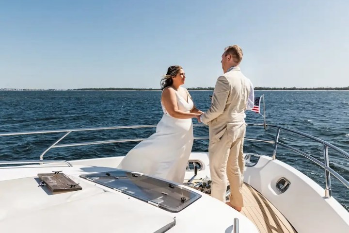 Couple holding hands on a boat deck during a sunny day with ocean in the background.