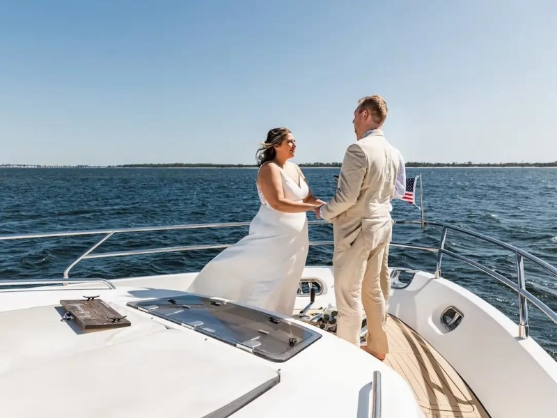 Couple holding hands on a boat deck during a sunny day with ocean in the background.