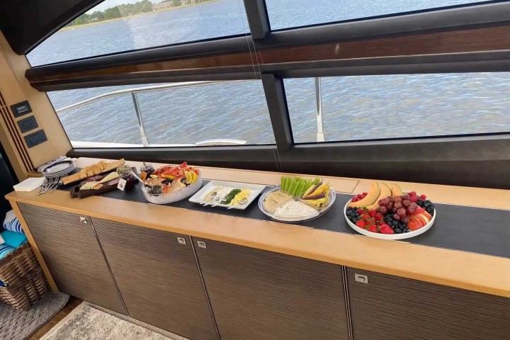 Buffet with fruits, vegetables, and snacks on a boat with a scenic water view through the window.