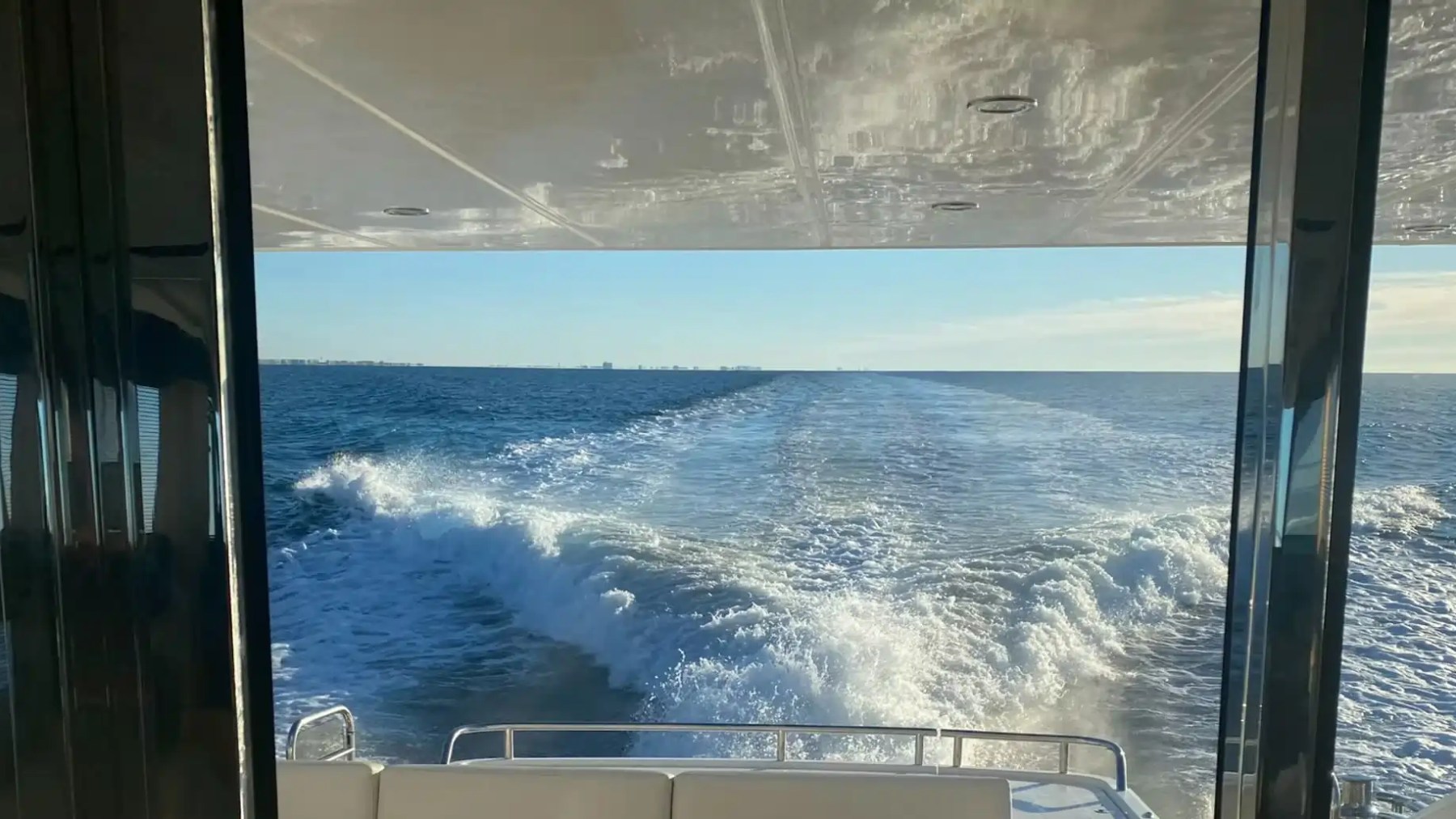 View from boat interior of ocean waves and horizon under clear sky.