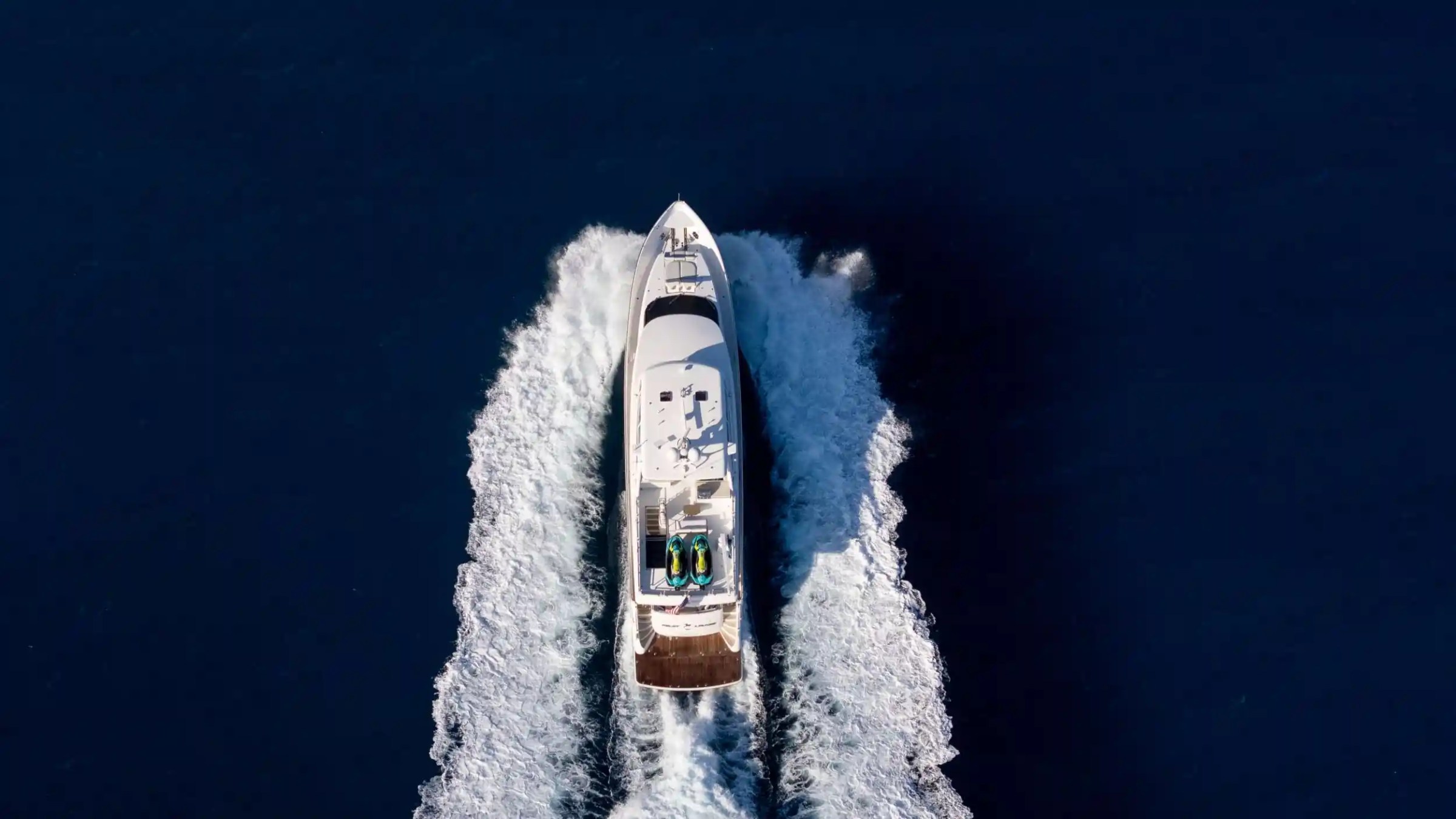 Aerial view of a white yacht sailing on deep blue water with trailing wake.