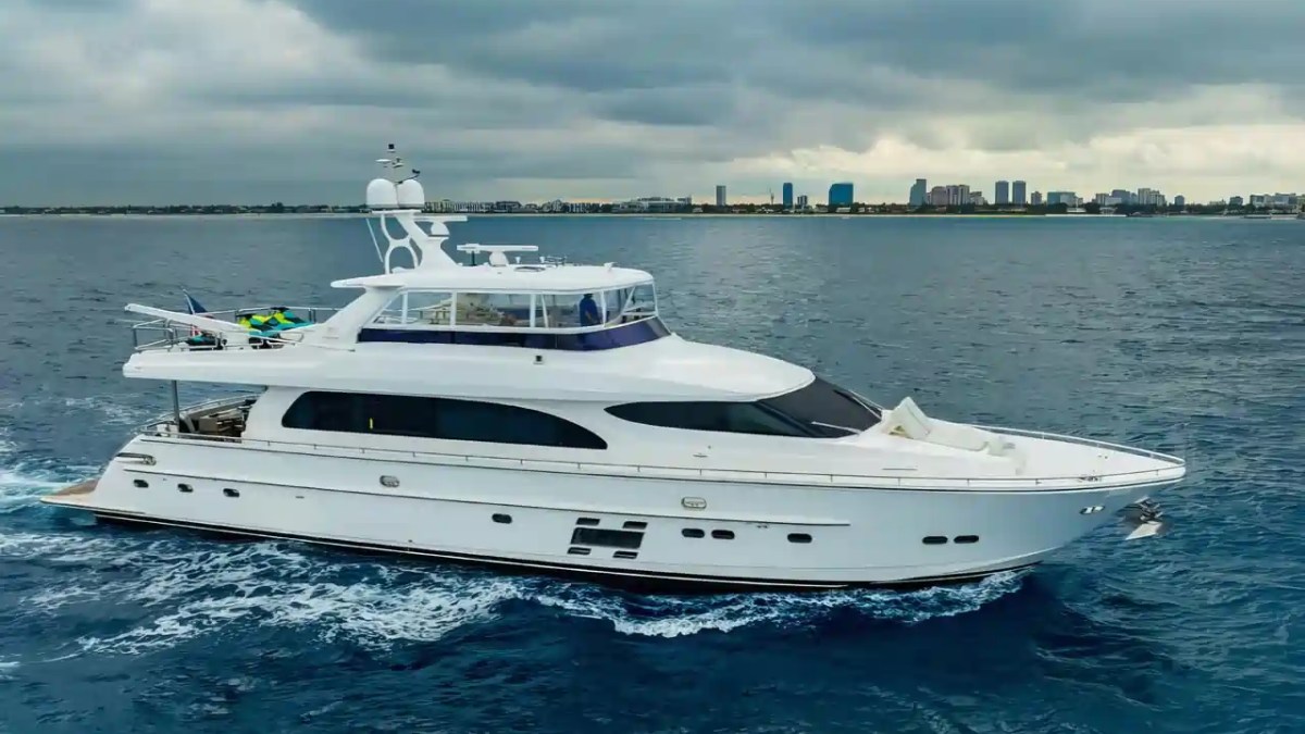 Large white yacht cruising on the ocean with city skyline in background.