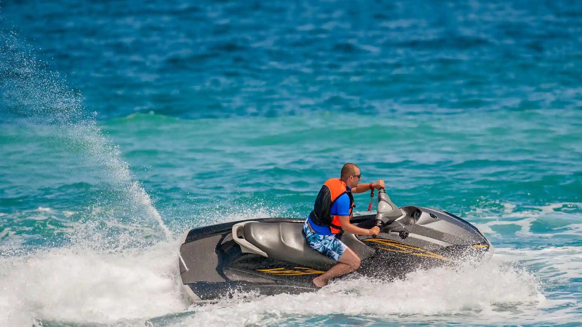 Person riding a jet ski in the ocean, wearing a life jacket on a sunny day.