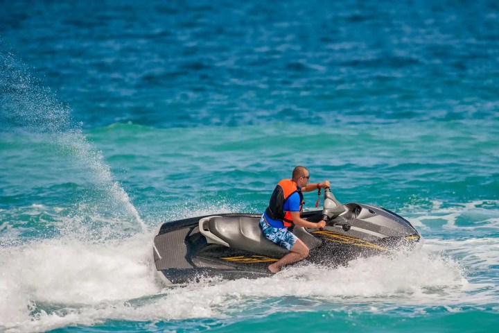 Person riding a jet ski in the ocean, wearing a life jacket on a sunny day.