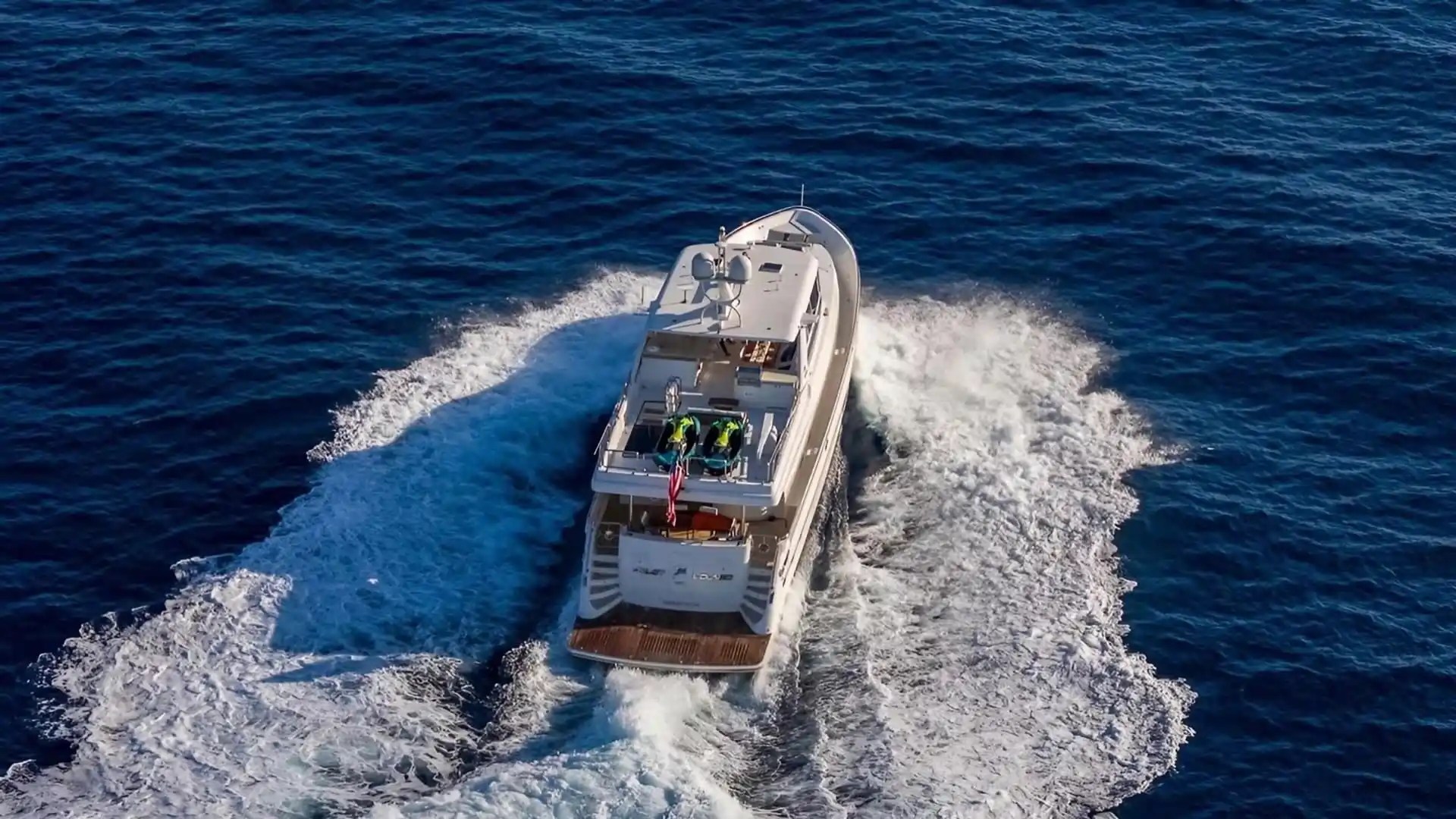 Aerial view of a yacht cruising through blue ocean water, leaving a trail of white waves behind.