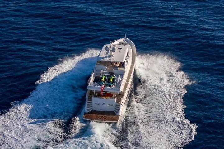 Aerial view of a yacht cruising through blue ocean water, leaving a trail of white waves behind.