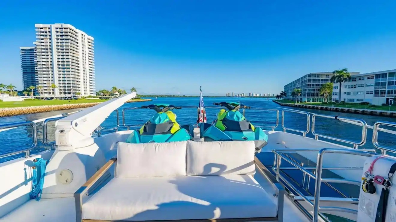 View from a yacht deck with jet skis, overlooking water and buildings under a clear blue sky.
