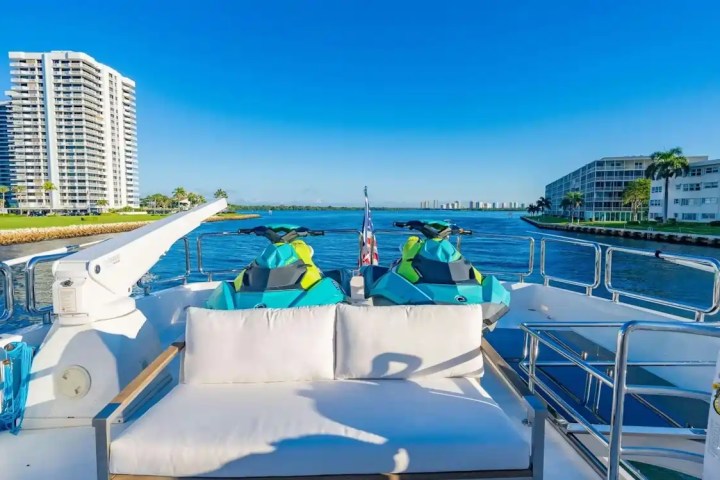 View from a yacht deck with jet skis, overlooking water and buildings under a clear blue sky.