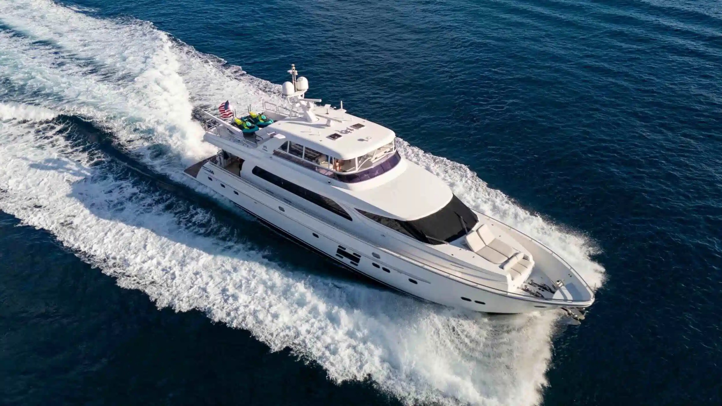 Aerial view of a white yacht cruising on blue ocean waters, leaving a wake behind.