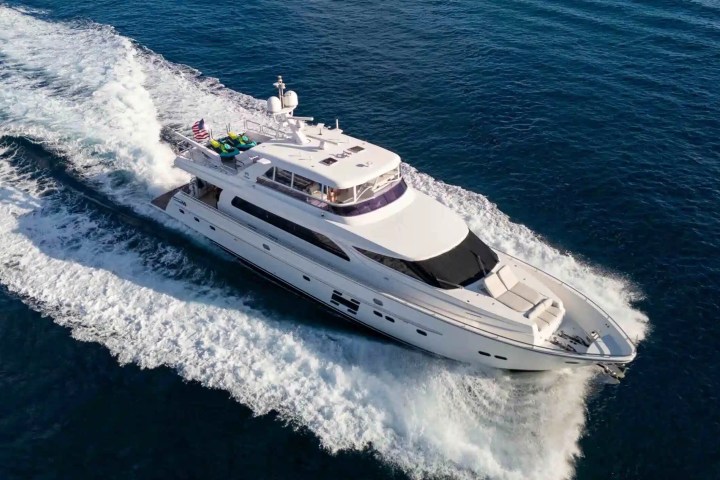 Aerial view of a white yacht cruising on blue ocean waters, leaving a wake behind.