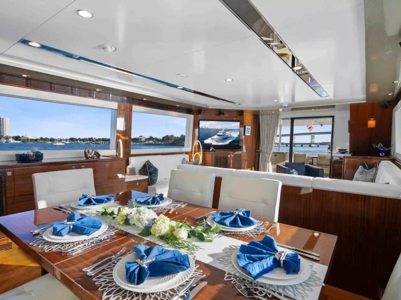 Elegant yacht interior with dining table set, white chairs, windows showing a harbor view.