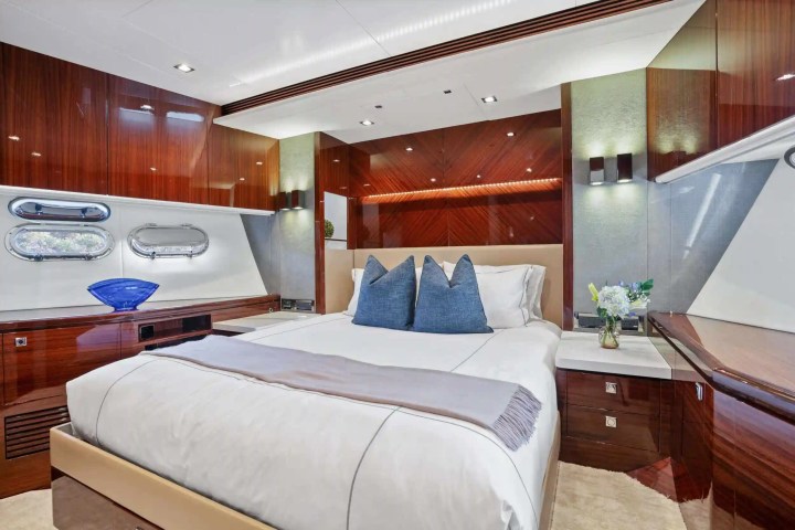 Luxurious yacht bedroom with wood paneling, bed, blue pillows, and decorative vase.