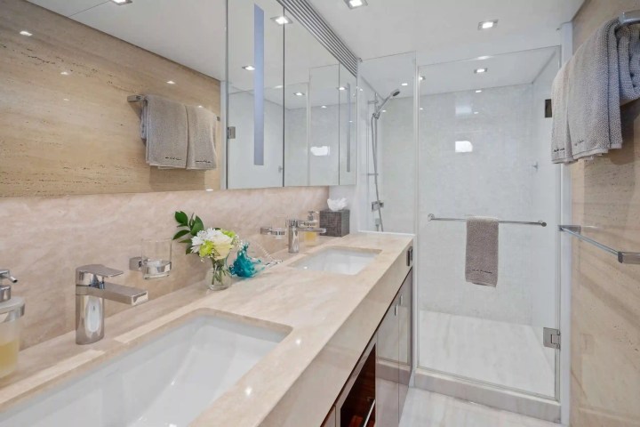 Modern bathroom with dual sinks, beige countertops, mirrored wall, and glass shower stall.