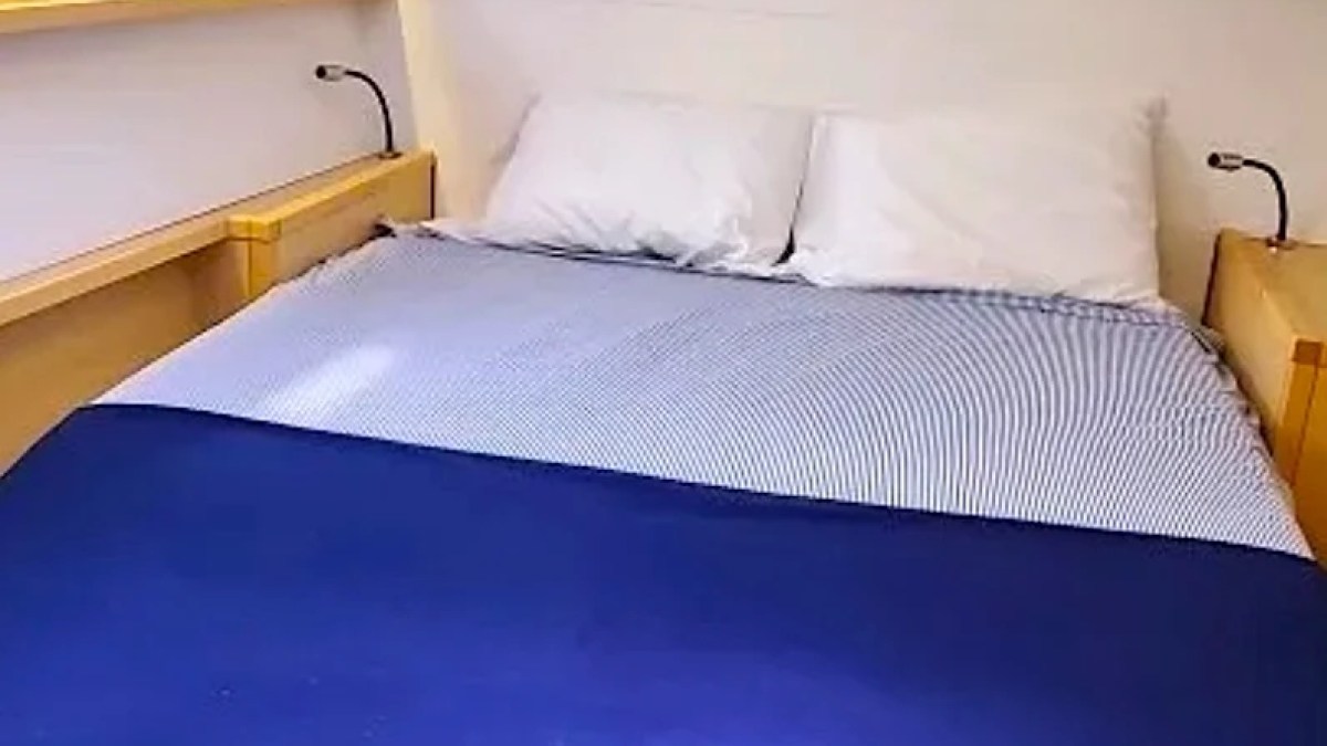 Compact bedroom with a bed, two pillows, porthole, and reading lights on a boat.