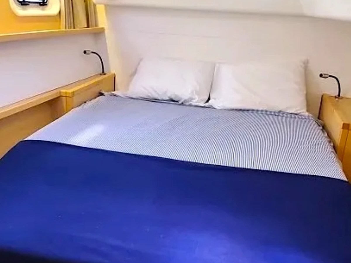 Compact bedroom with a bed, two pillows, porthole, and reading lights on a boat.