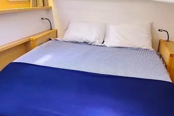 Compact bedroom with a bed, two pillows, porthole, and reading lights on a boat.