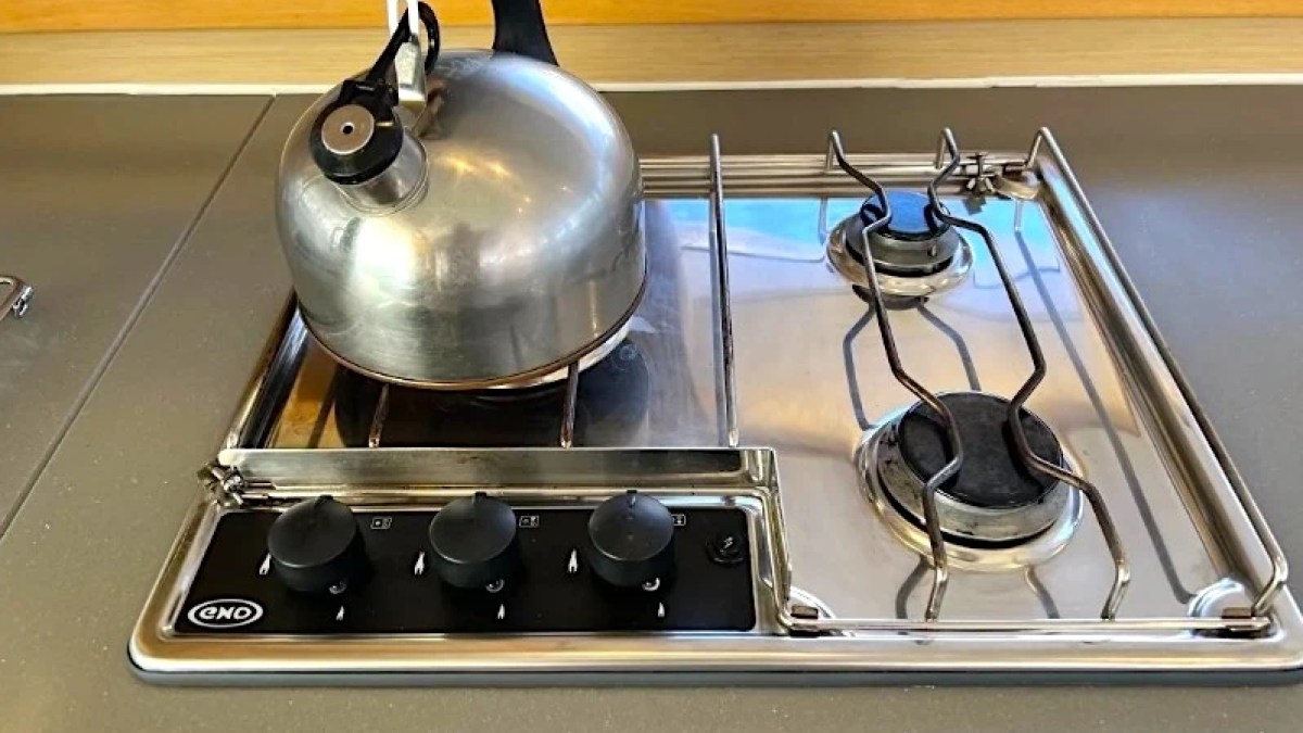 Metal kettle on a gas stovetop with two burners and control knobs.