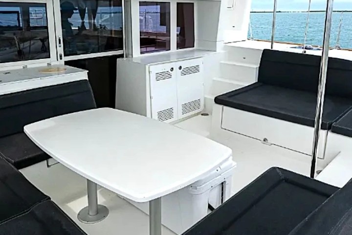 Interior of a yacht's deck with white table, black seating, and ocean view.