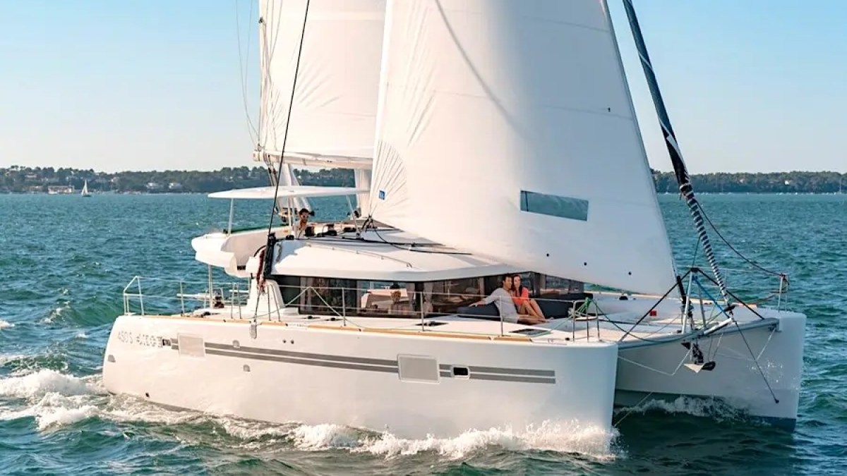 Catamaran with white sails on open water under blue sky.