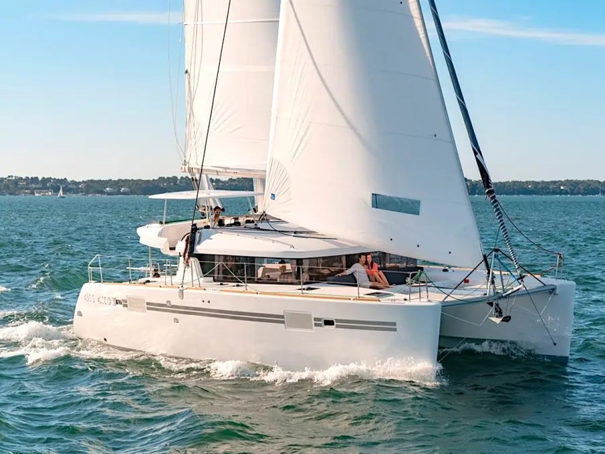 Catamaran with white sails on open water under blue sky.